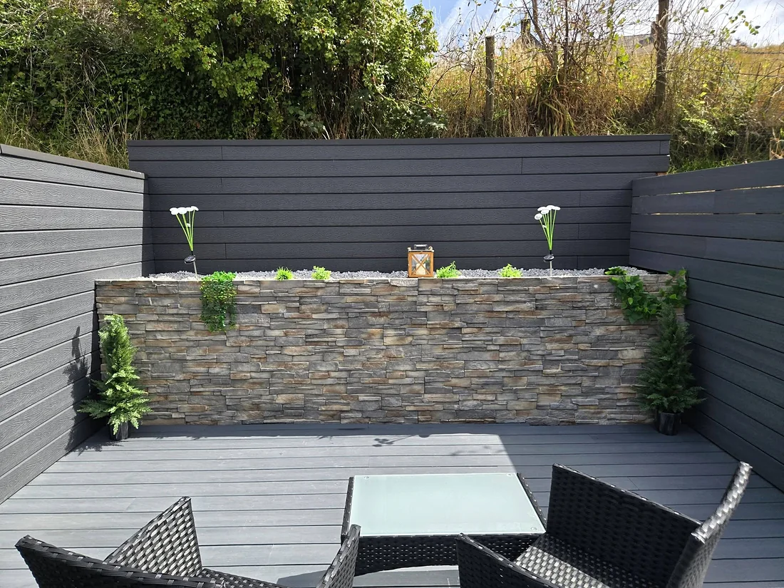 Grey composite deck and cladding round a stone-faced planter wall with seating