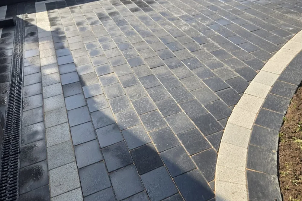 Charcoal block-paved path with a light grey border curving round a lawn